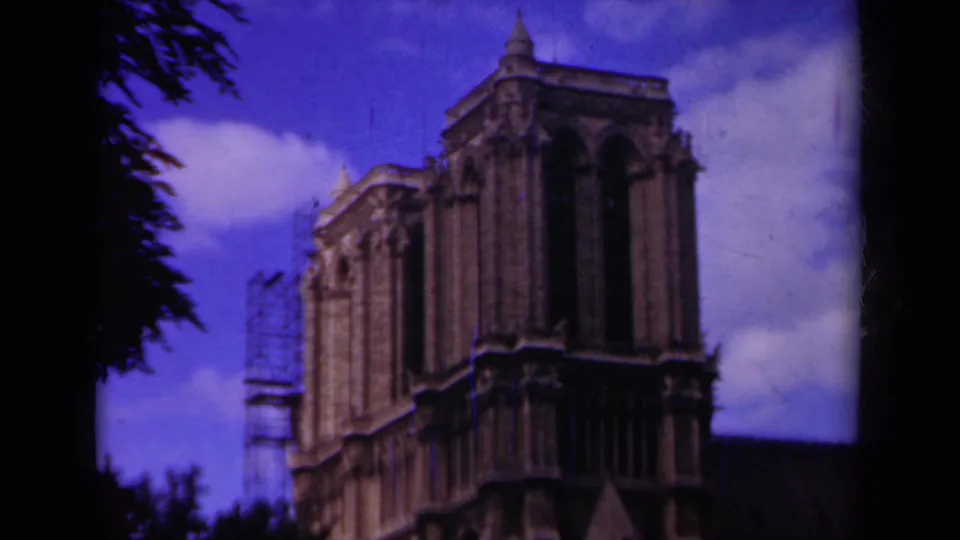 1939 Paris 8mm frame showing Notre-Dame Cathedral's tower and rear stone facade, with scaffolding, clouds, and dark tree edges.