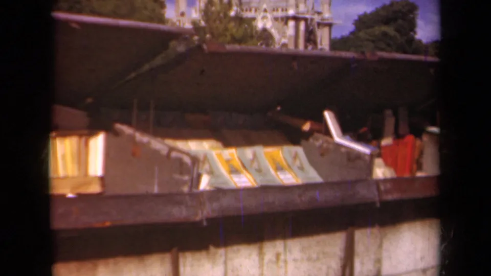 1939 Paris 8mm frame showing a metal container filled with books, papers, and indistinct discarded objects beside a wall.