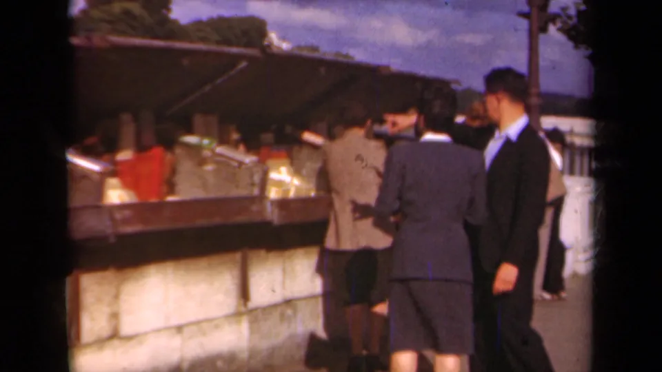 Paris, 1939 footage shows suited adults near a canopy-covered outdoor vendor stall with goods arranged on shelves.