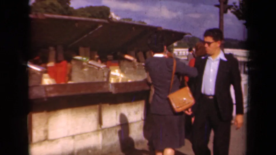 Paris, 1939 footage shows a man in sunglasses walking past adults gathered at a canopy-covered outdoor market stall.