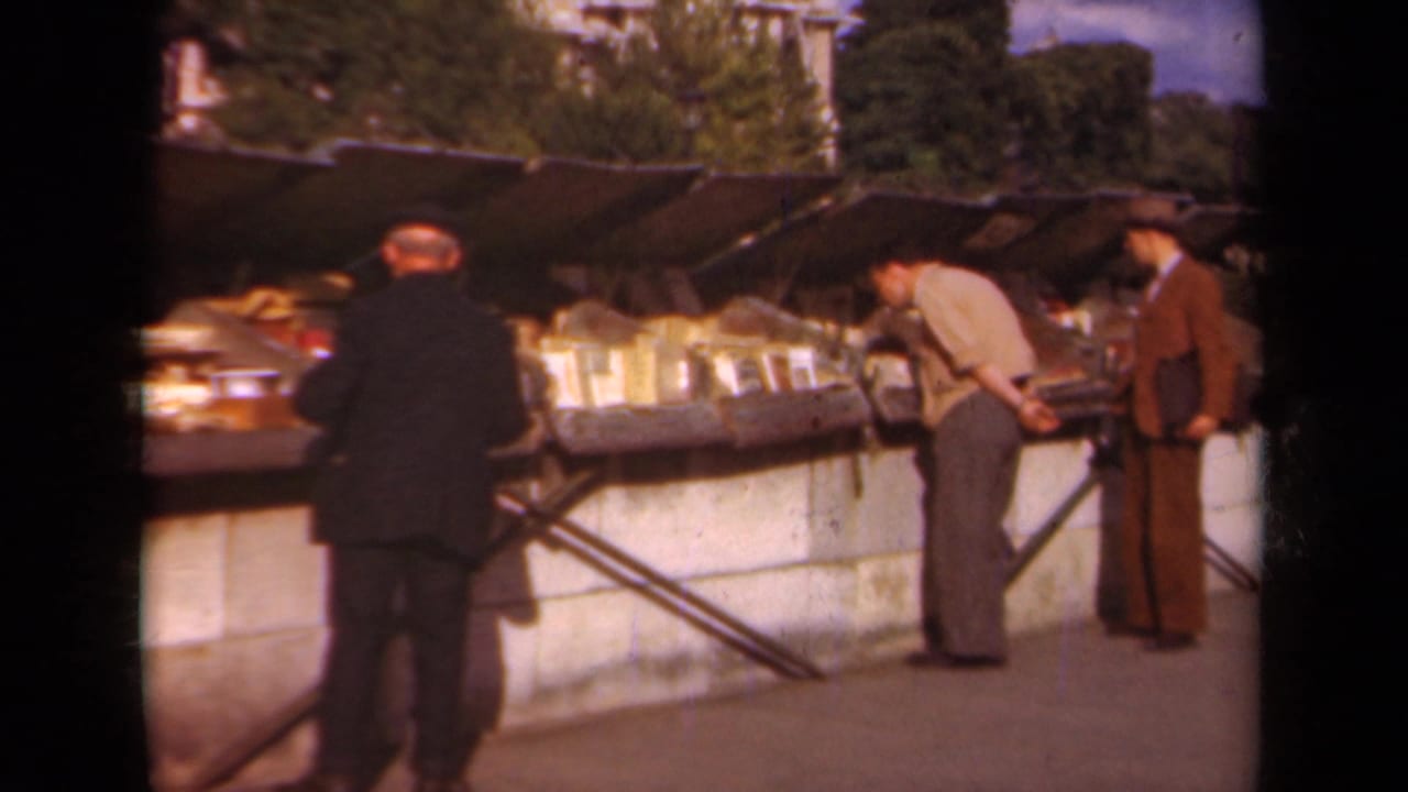 Three men stand near open book tables under market canopies.