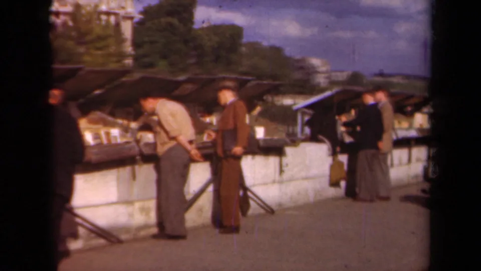 Late-1930s Paris street scene showing men gathered at outdoor book tables under canopies.