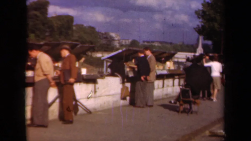 1939 Paris street-market scene with suited men near stalls, a stroller, and pedestrians farther down the promenade.