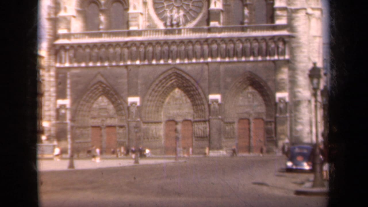 Notre Dame facade with pedestrians and a dark car near the plaza edge.