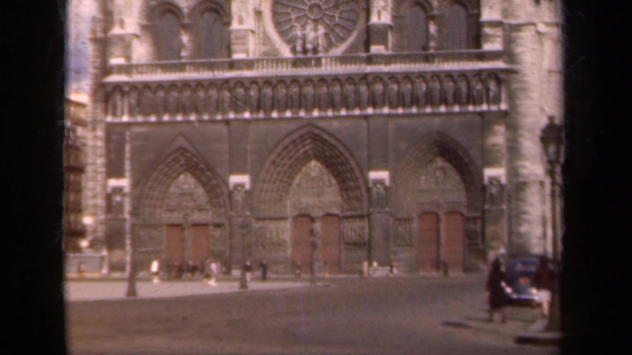 Cathedral entrance area with small pedestrians and a car at right.