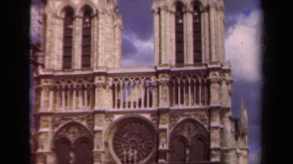 1939 Paris frame showing Notre-Dame's upper facade, tower openings, rose window, and clouds beyond the stonework.