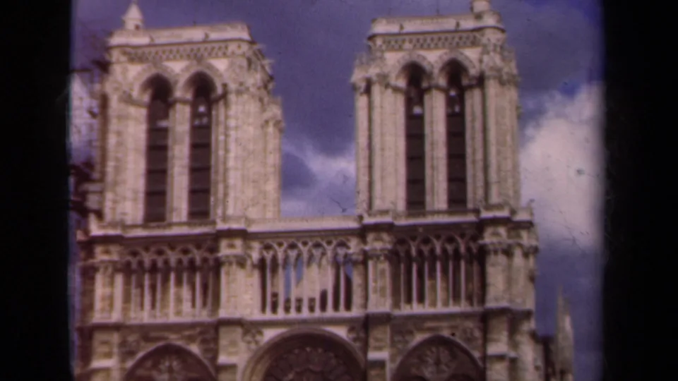 1939 Paris home-movie frame featuring Notre-Dame's twin towers, upper gallery, rose window, and partly cloudy sky.