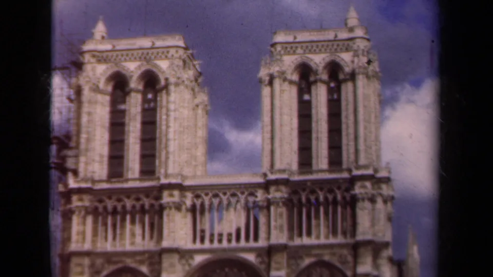 1939 Paris home-movie frame showing Notre-Dame Cathedral's twin towers, Gothic facade details, blue sky, and maintenance scaffolding at left.