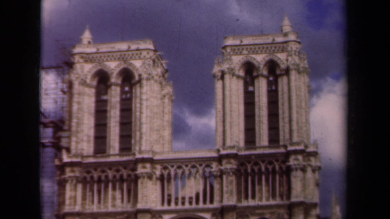 Paris frame of Notre-Dame Cathedral in 1939, with twin towers, upper Gothic facade, blue sky, clouds, and side scaffolding visible.