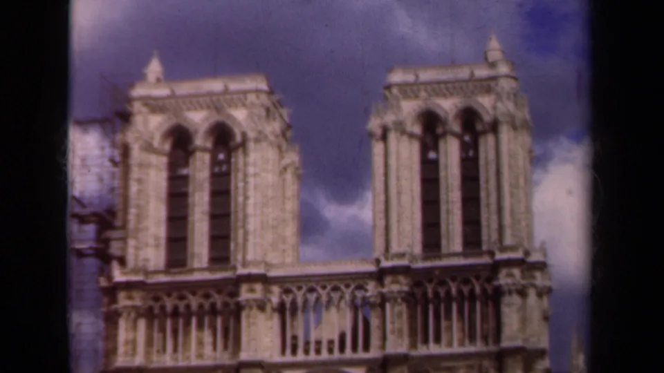 1939 Notre-Dame Cathedral view from Paris, showing the twin towers, ornate stonework, blue sky, and soft 8mm film texture.