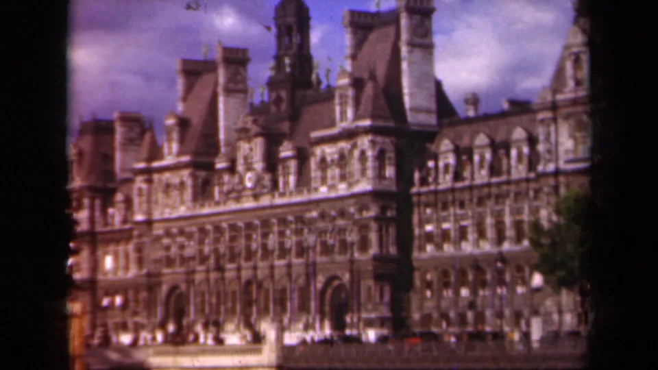 1939 Paris view of the Hôtel de Ville facade with towers, arched entrances, rooflines, and cloudy sky in soft 8mm color.