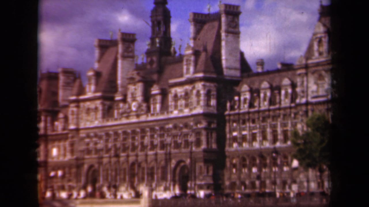 The Paris Hôtel de Ville appears in a soft 1939 8mm frame, with its civic facade, roof towers, and a dark tree edge visible.