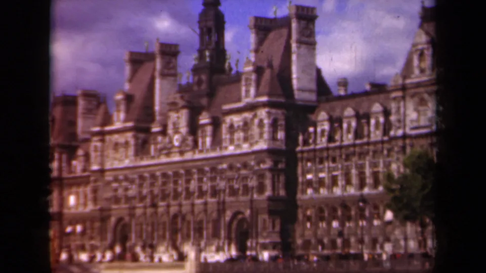 The Paris Hôtel de Ville appears in a soft 1939 8mm frame, with its civic facade, roof towers, and a dark tree edge visible.