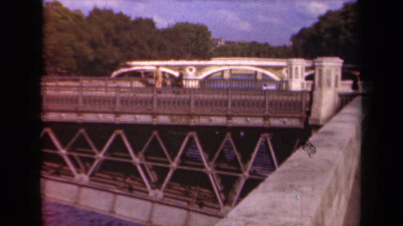 Metal truss bridge over water with pedestrians crossing and trees beyond.