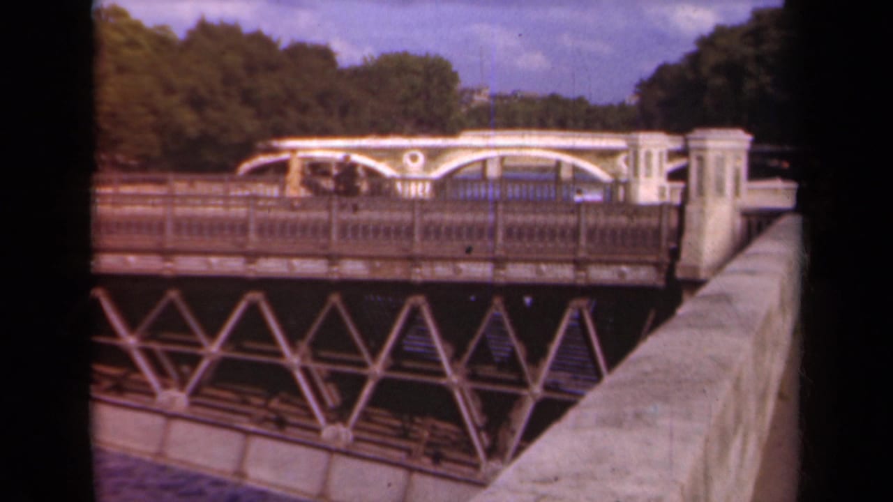 Paris bridge view from the 1939 8mm clip, showing the trusswork, railing, water edge, and trees beyond.