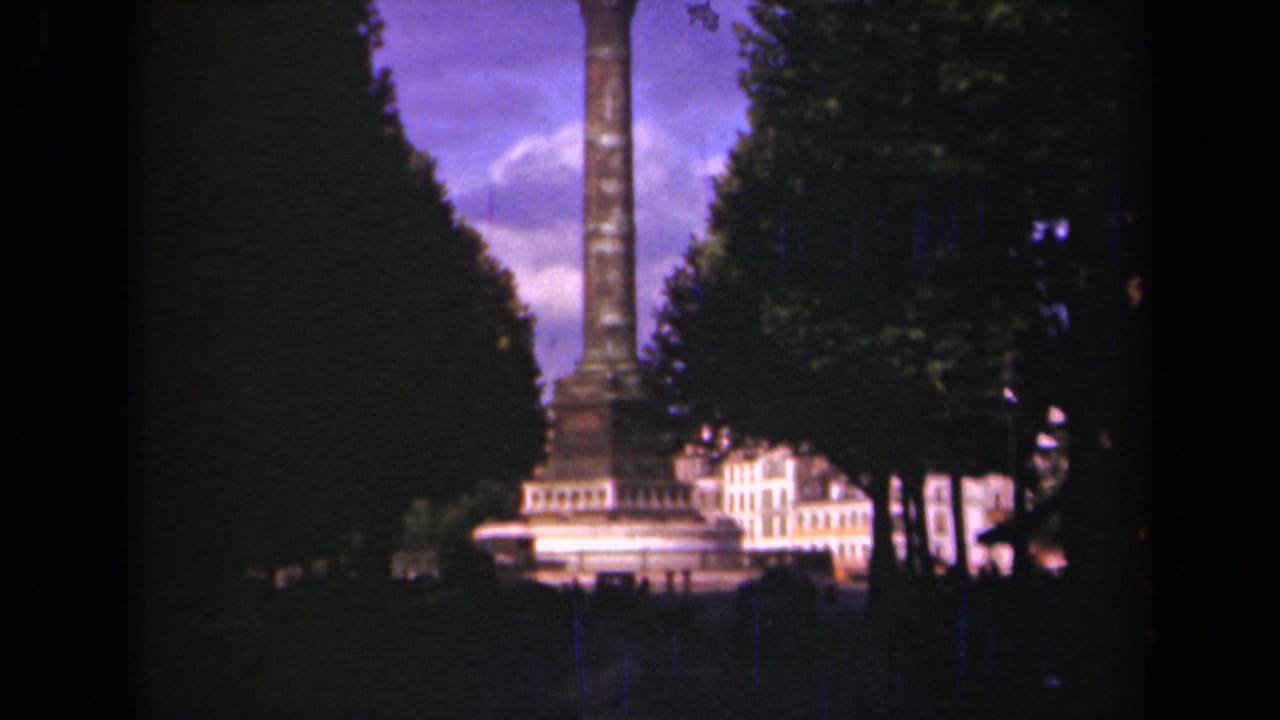 1939 Paris home-movie view of a tall column monument seen between rows of trees, with bright buildings at its base.