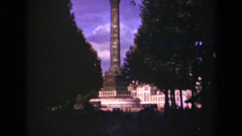 1939 Paris home-movie view of a tall column monument seen between rows of trees, with bright buildings at its base.