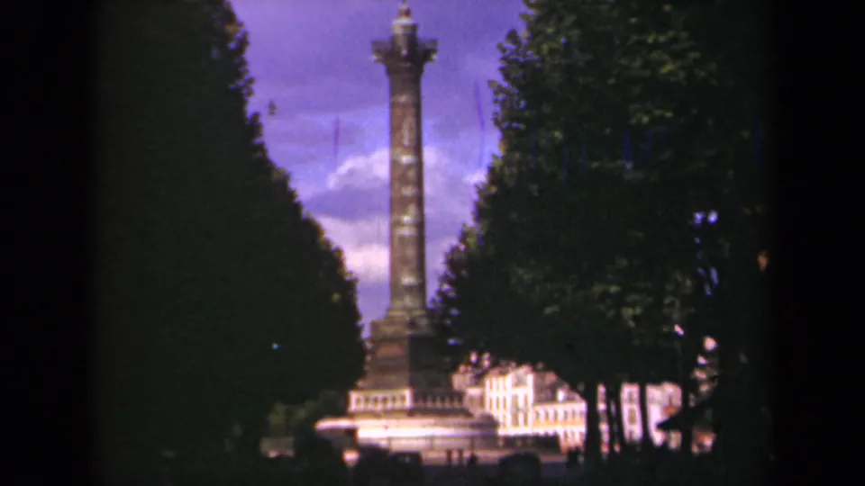 1939 Paris frame with a tall column and statue, bordered by dense trees and backed by light-colored urban buildings.