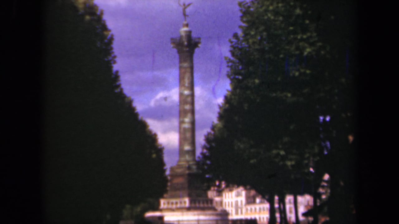 1939 Paris home-movie view of the column monument, with the statue top silhouetted against a purple sky and trees at both sides.