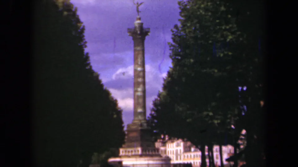 1939 Paris home-movie view of the column monument, with the statue top silhouetted against a purple sky and trees at both sides.