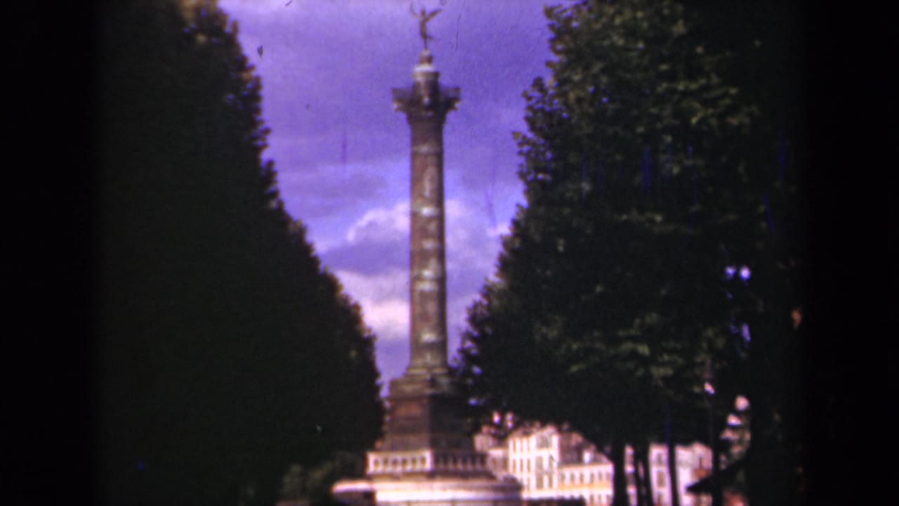 Column monument and statue centered between trees with bright clouds behind it.