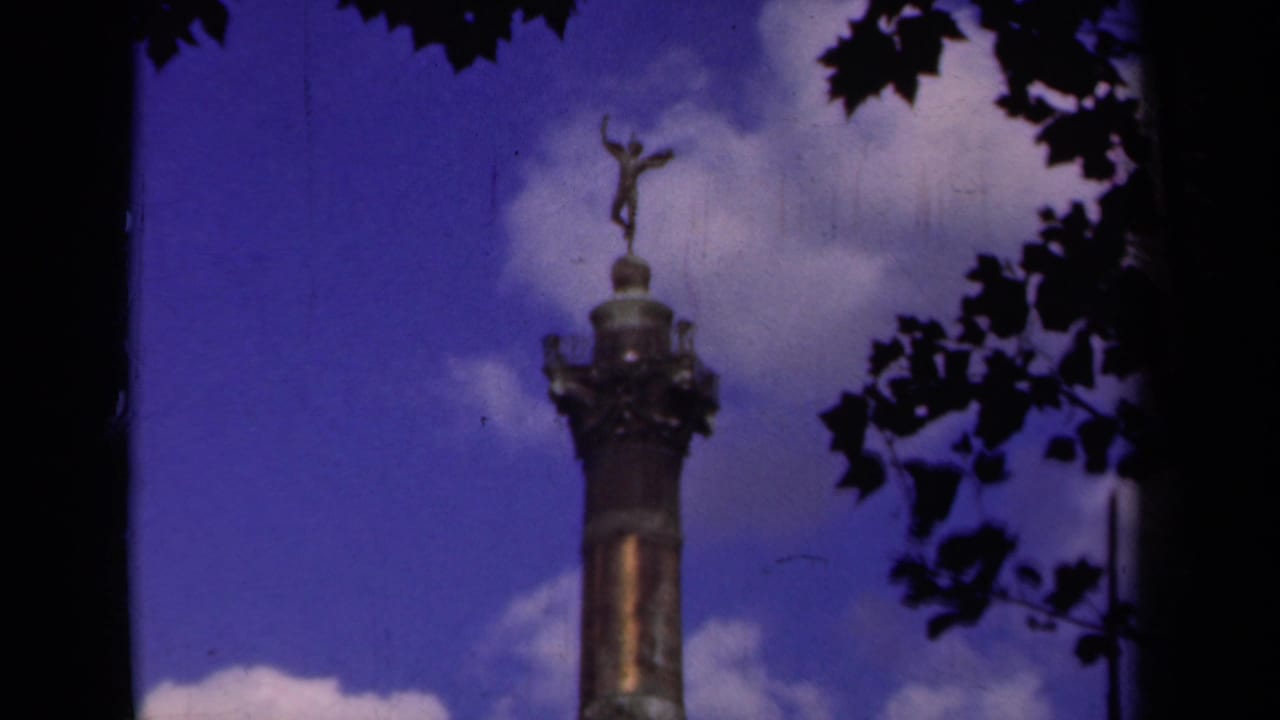 Bronze monument top with winged figure framed by dark leaves and bright clouds.