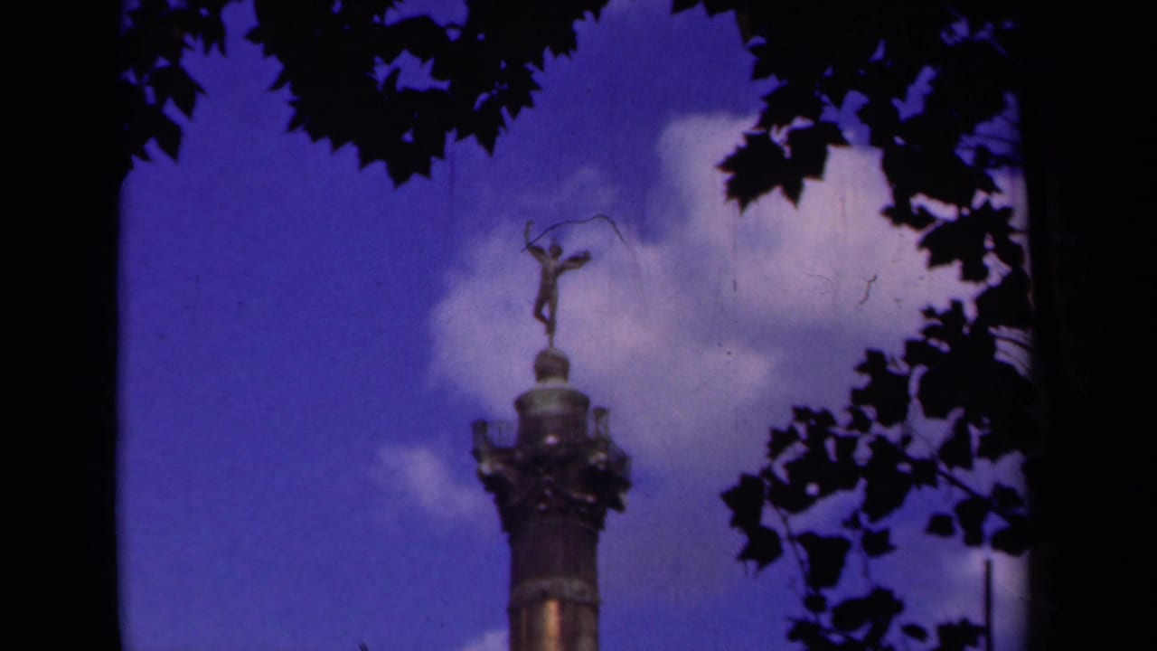 Final 1939 Paris 8mm frame showing the winged statue atop the column with sky, clouds, and dark foliage.