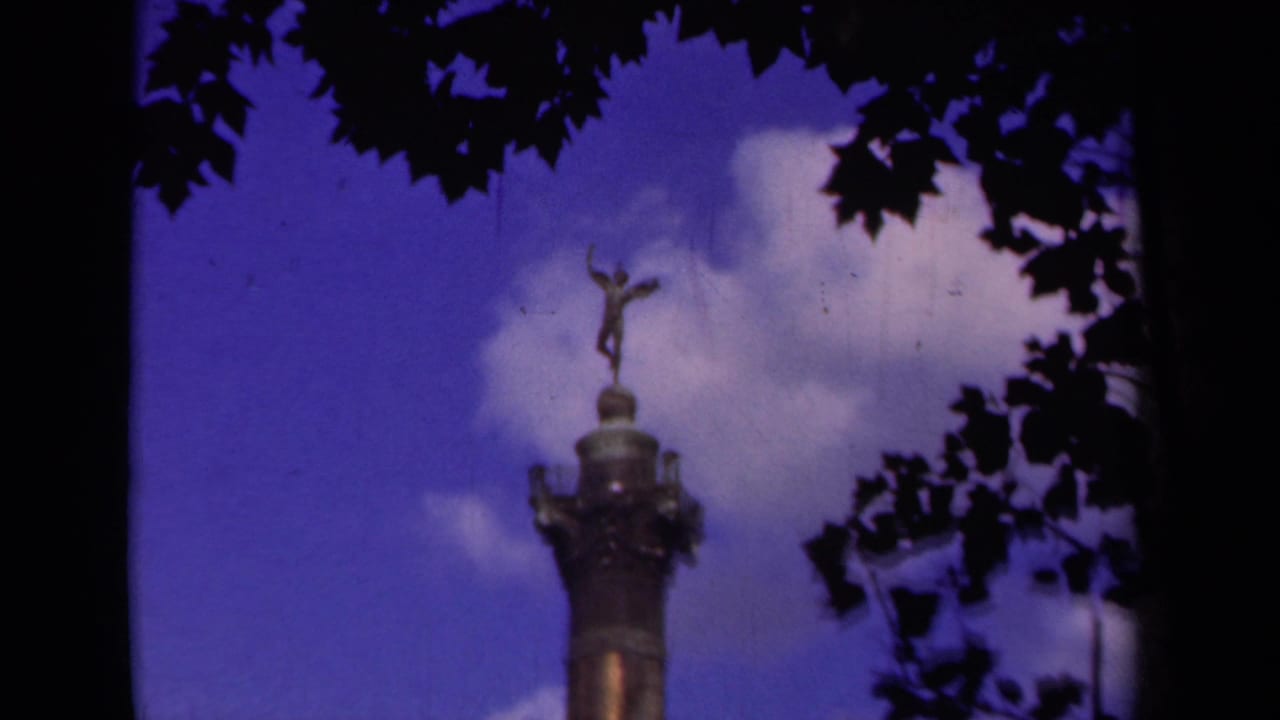 1939 Paris 8mm frame showing the upper Arc de Triomphe area framed by silhouetted tree leaves and a deep blue sky.