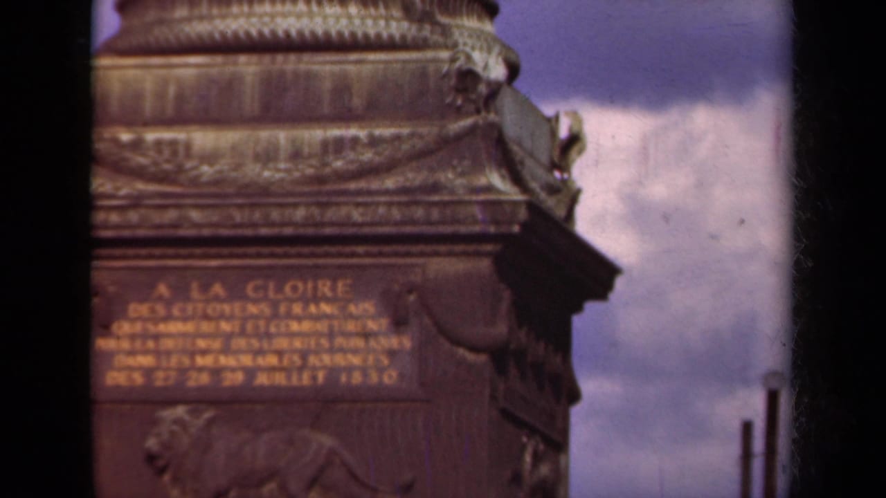 1939 Paris 8mm frame showing an inscribed monument base with decorative carving, a bronze relief, and cloudy sky behind it.