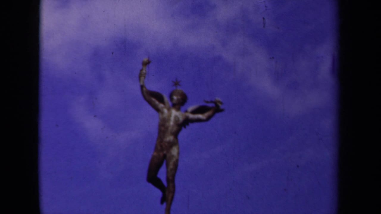 1939 Paris 8mm frame with a winged statue silhouetted against a saturated blue-purple sky and visible film wear.