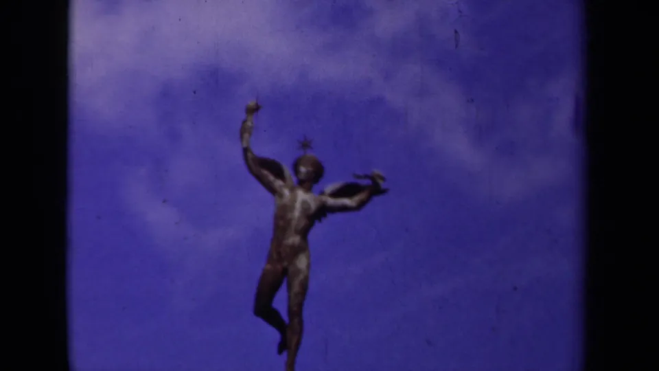 1939 Paris 8mm frame with a winged statue silhouetted against a saturated blue-purple sky and visible film wear.