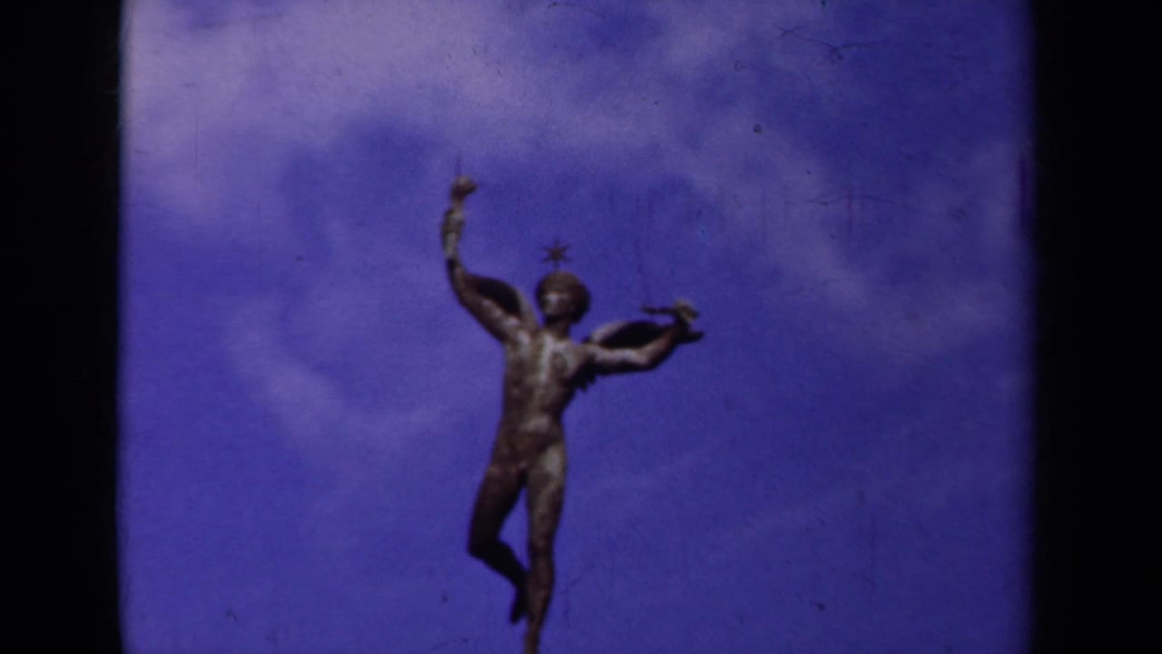 1939 Paris home-movie frame showing a winged bronze male statue with one arm raised against a blue sky.