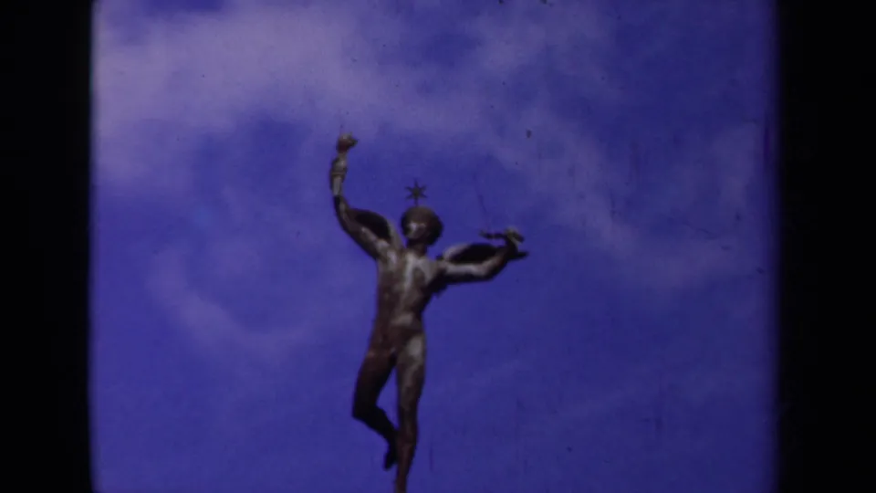 1939 Paris home-movie still of a bronze winged figure beneath drifting clouds, with visible grain and color shift.