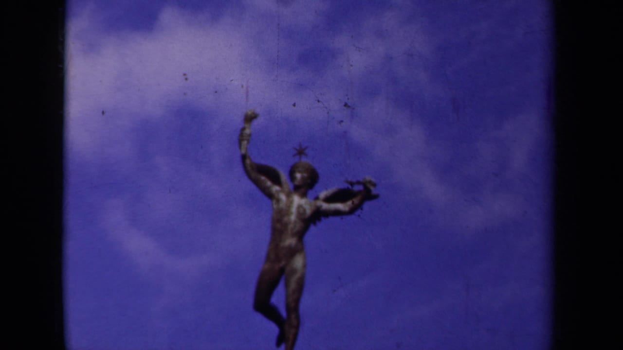 Final 1939 Paris frame showing the winged male statue silhouetted against saturated blue sky and pale clouds.