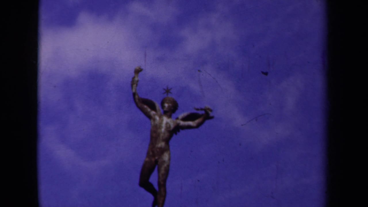 1939 Paris frame of a classical winged nude figure standing above a bridge, seen in soft color 8mm footage.