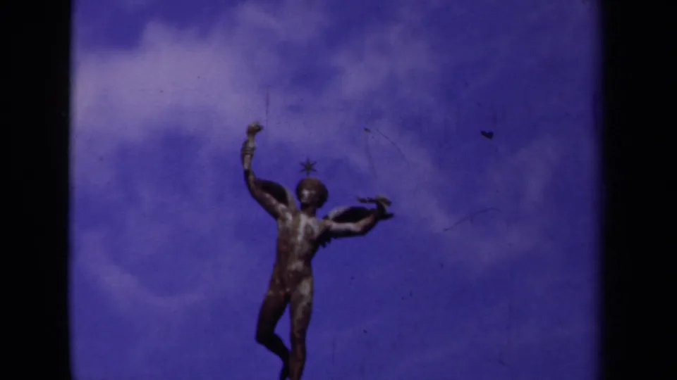 1939 Paris frame of a classical winged nude figure standing above a bridge, seen in soft color 8mm footage.