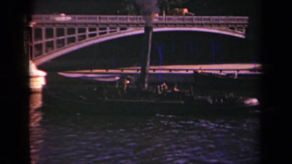 1939 Paris home-movie frame showing a boat under an arched bridge, with bright light reflections on the river surface.
