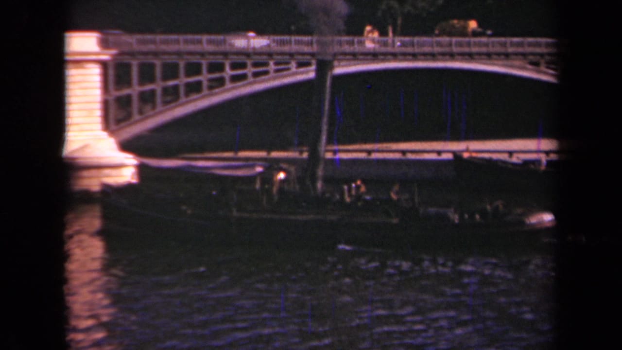 Illuminated arched bridge over dark water with a passenger barge below.