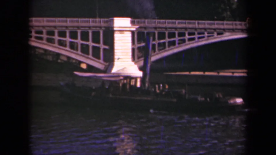 Final frame of the Paris night river view, with the bridge glowing above a dark passenger barge and rippled water reflections.