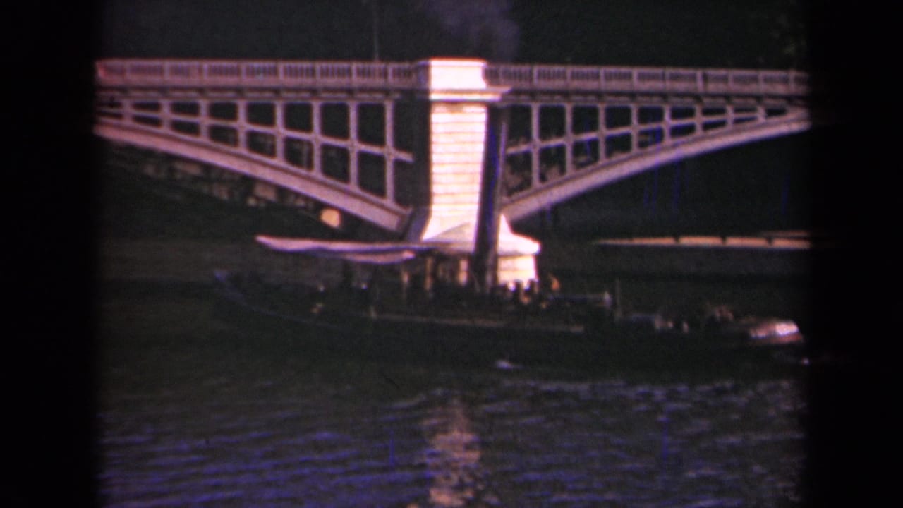 1939 Paris home-movie frame showing a steam boat beneath an arched bridge, with dark smoke rising and water in the foreground.