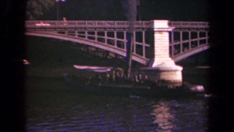 A 1939 Paris frame with passengers visible on a small river boat beside a stone bridge pier as smoke drifts upward.