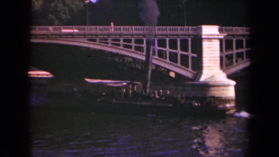 Late-1930s Paris home-movie view of a small boat below an arched bridge, with smoke and rippled river water in frame.