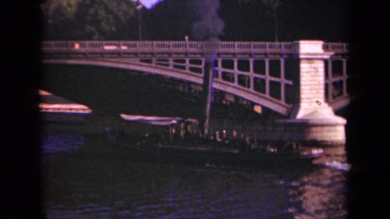1939 Paris 8mm frame showing a river boat near a stone arch bridge, with pedestrians along the railing and trees beyond.