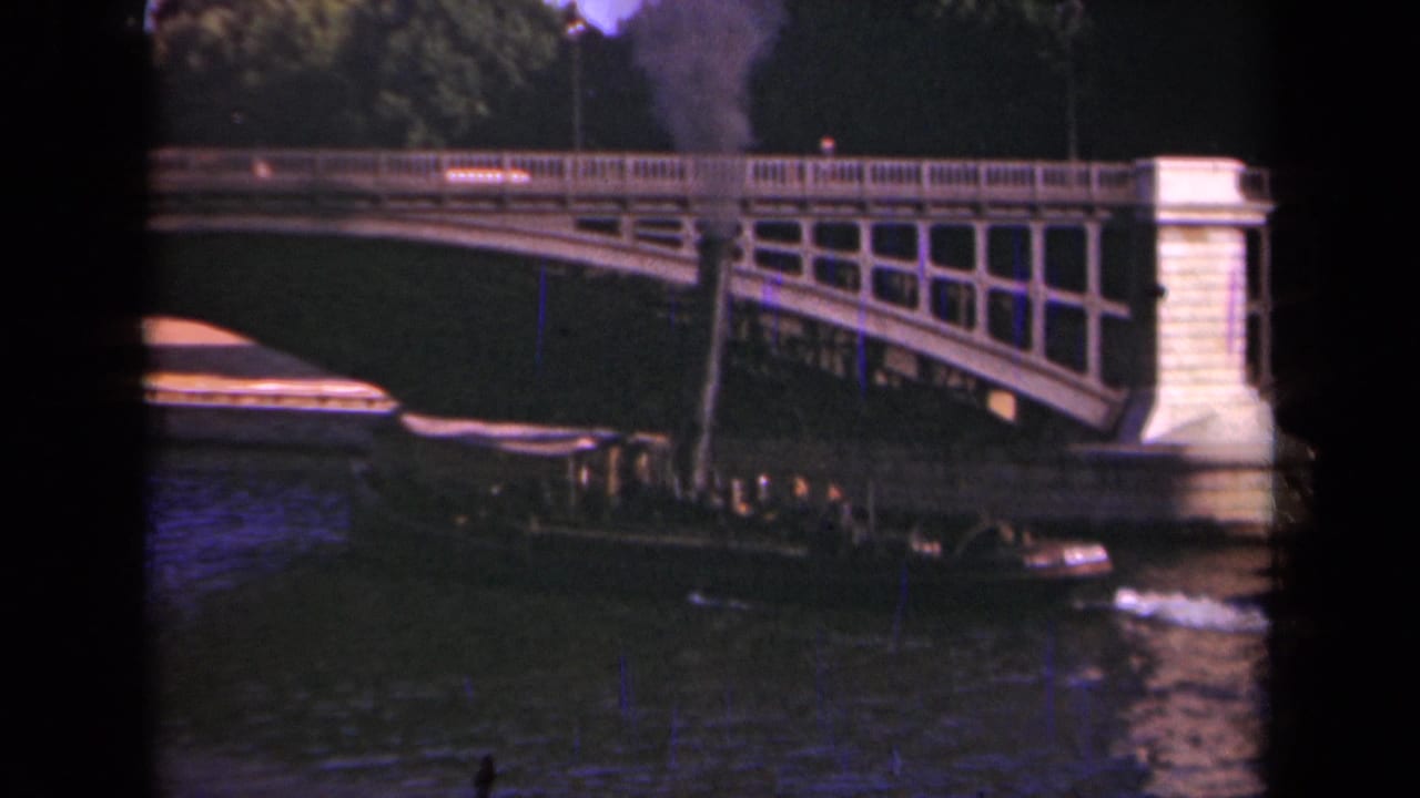 1939 Paris home-movie frame with a smoking river boat under a stone bridge and small pedestrian figures crossing above.