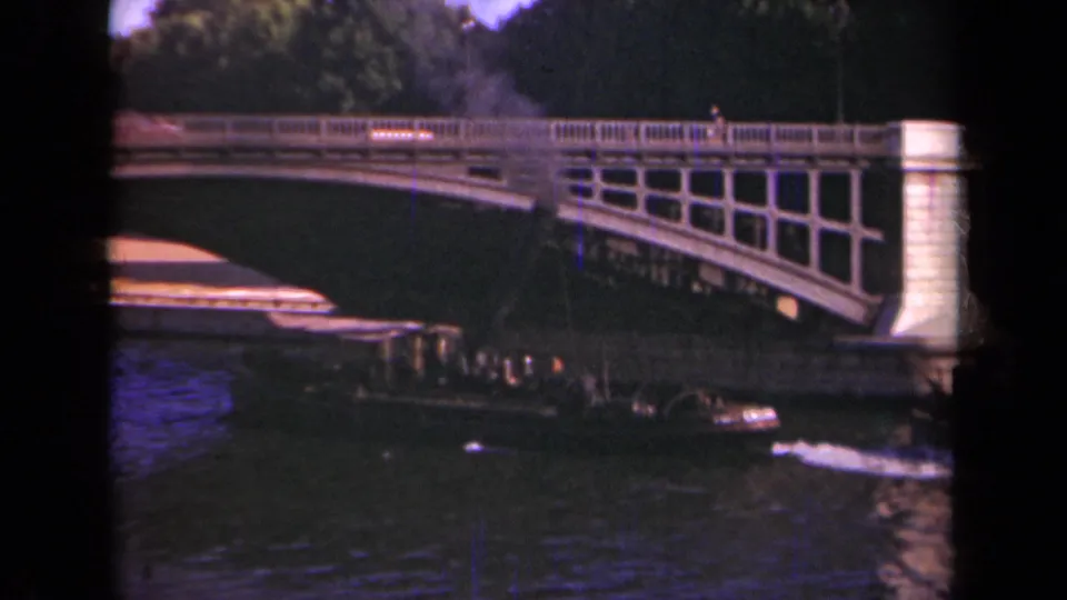 Paris 1939 8mm frame showing the boat partly under the bridge, with the stone pier, railing, water, and distant pedestrians visible.