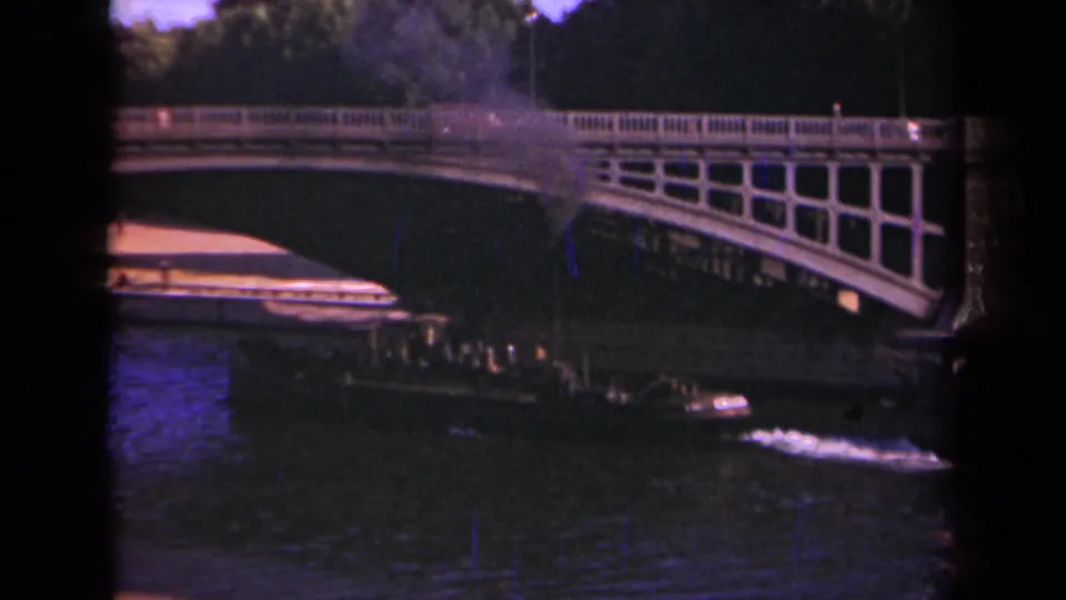 Final 1939 Paris frame with the river boat emerging near the bridge shadow, leaving wake beneath pedestrians on the bridge.