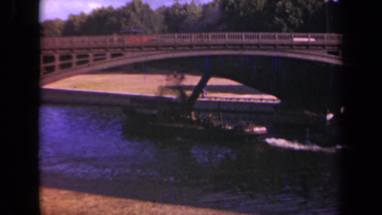 1939 Paris frame with a small vessel passing beneath a bridge, its wake visible against the dark river water.