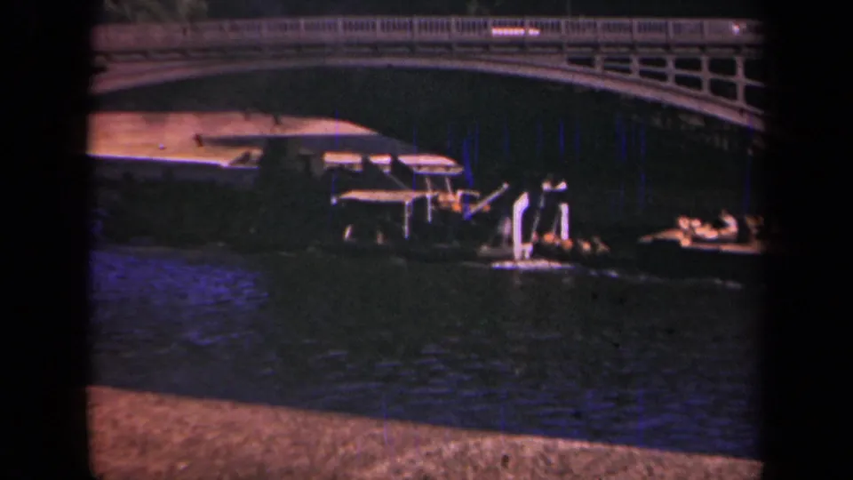 1939 Paris frame showing a riverboat under the bridge with railings above and small indistinct people near the shaded river edge.