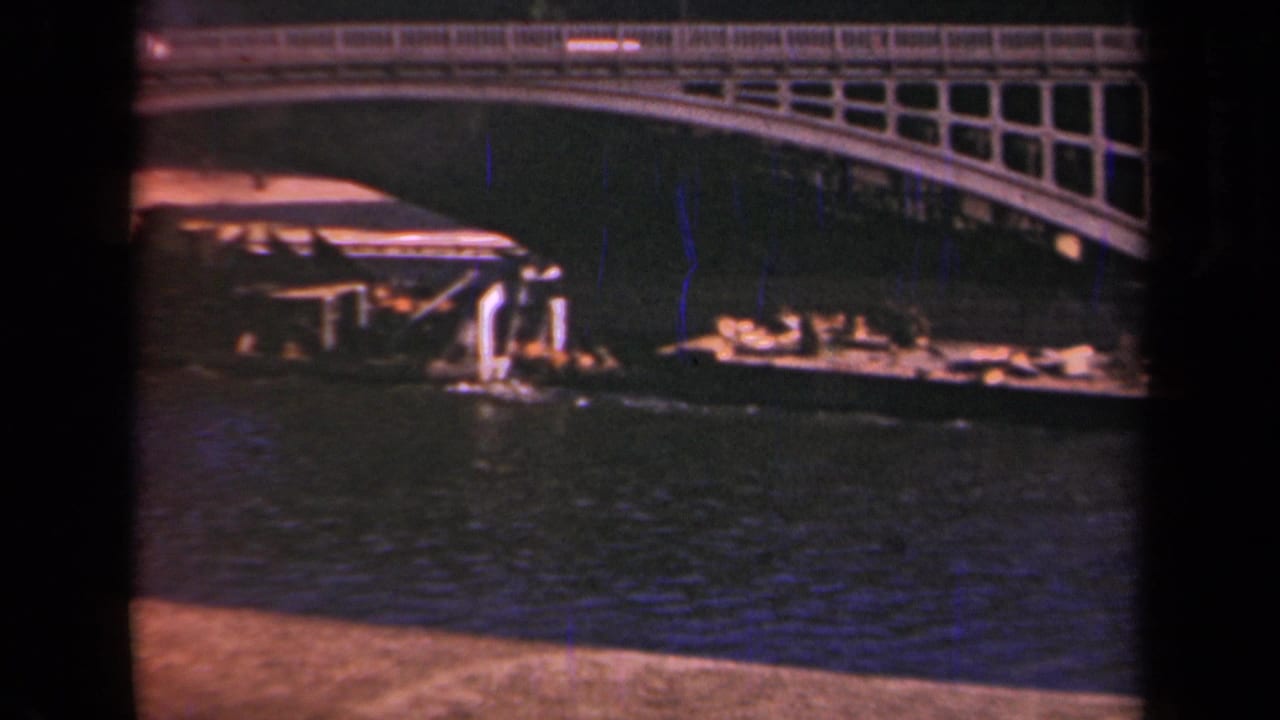 1939 Paris frame with a low boat or barge moving near an arched bridge over rippled water.