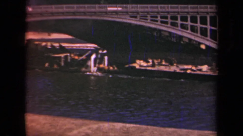 1939 Paris frame with a low boat or barge moving near an arched bridge over rippled water.